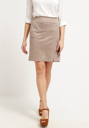 Femme portant une jupe beige mi-longue avec une petite fente à l'avant, une chemise blanche à manches longues et des sandales plates-formes marron à talons hauts, marchant vers l'avant.