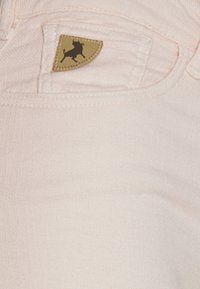 Svetle růžové džíny s texturovanou tkaninou, se hnědou koženou etiketou s černým siluetou býka na přední kapse.