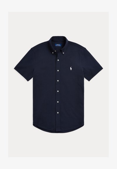Camicia blu navy a maniche corte in cotone con bottoni; presenta un orlo curvo e un piccolo logo bianco sul petto a sinistra con dettagli a bottoni.