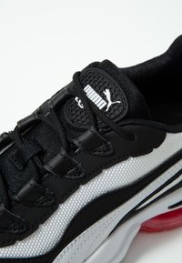 Sneakers noir et blanc avec un upper en mesh texturé, une languette rembourrée, des lacets noirs et une semelle en caoutchouc avec des accents rouges. Logo sur la languette.