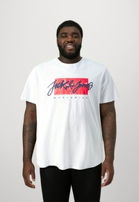 White cotton t-shirt featuring a red and blue graphic print with "Jack & Jones" and "WORLDWIDE" text. Relaxed fit with short sleeves.