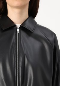 Giubbotto in pelle nera con colletto affilato, chiusura con zip e texture liscia, che evidenzia un design elegante e aderente.