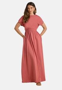 Robe maxi dans une douce teinte corail, avec des manches courtes, une taille élastique et des poches latérales, fabriquée en tissu léger.