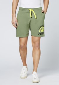 Olivgrüne Baumwollshorts mit einem gelben Kordelzug, Seitentaschen und schwarzem Text/Logo am linken Bein. Glatte Textur, lässiges Design.