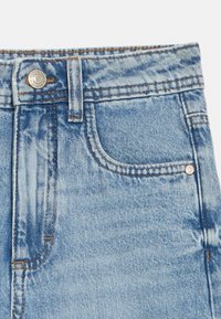 Helelehadesinine kõrge vöökohaga teksad helesinises toonis, millel on tavaline tasku, metallist nööp ja kontrastse oranži õmblusdetailid õmbluste ääres.