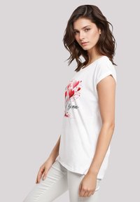 White cotton t-shirt featuring a graphic of red hearts and the text "Be mine." Short sleeves and a relaxed fit.