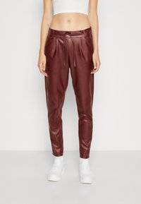 Joggers en similicuir marron bordeaux avec une coupe décontractée, taille à cordon, jambes fuselées et plis avant, associés à des baskets blanches.