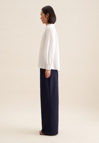 Blusa bianca a maniche lunghe con maniche a palloncino abbinata a pantaloni navy a vita alta e a gamba larga. Texture morbide e silhouette rilassata.