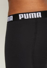 Black boxer shorts with a wide elastic waistband featuring "PUMA" in bold white letters. Smooth texture, fitted design, and neat stitching.