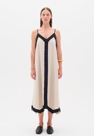 Ärmelloses Kleid aus Leinenmischung in Beige mit schwarzen Akzenten, mit V-Ausschnitt, seitlichen Schlitzen und schwingendem Saum, kombiniert mit schwarzen Slippern.