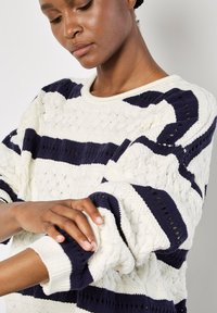 Gestrickter Pullover mit einer cremefarbenen Basis und marineblauen horizontalen Streifen, strukturierten Mustern und gerippten Bündchen. Solider runder Halsausschnitt.