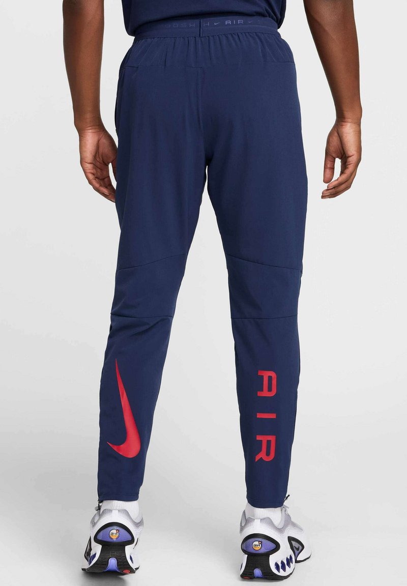 Granatowe spodnie sportowe o tapered designie, z czerwonym logiem Nike oraz napisem "AIR" wydrukowanym na boku w wyraźnym czerwonym kolorze.