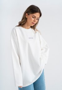 Witte sweatshirt met lange mouwen en een ontspannen pasvorm, voorzien van een ronde hals en het woord "MIRONS" geborduurd in lichtblauw. Zacht katoenmateriaal.