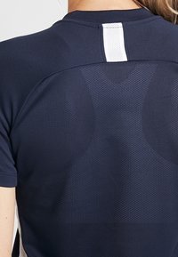 Námořnické sportovní tričko s texturovaným zadním dílem, obsahující síťovanou část a bílý akcentní pruh blízko krku. Krátké rukávy, přiléhavý střih.