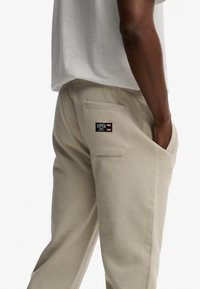 Beige Jogginghose aus weichem Stoff, mit einer Gesäßtasche und einem Logo-Patch. Gerader Schnitt mit elastischem Bund für Komfort.