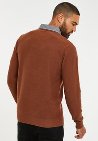 Brauner Strickpullover mit rundem Ausschnitt, gerippten Bündchen und Saum. Verfügt über einen karierten Kragen darunter, der von hinten sichtbar ist.