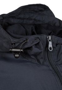 Marinblå vattentät jacka med hög krage, justerbar dragsko med stopper och en sidoketsj med metallisk hårdvara. Slät textur.