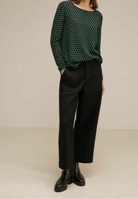 Long-sleeve green top with a hexagonal pattern, paired with high-waisted black trousers and black ankle boots.