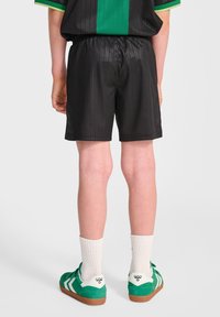 Svarta randiga shorts med elastisk midja, parat med gröna och vita sneakers och ljusa strumpor.