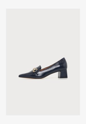 Chaussure en cuir noir brillant à petit talon bloc, bout pointu avec boucle décorative dorée sur le dessus, vue de côté sur fond blanc.