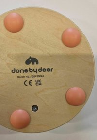 Base circular de madera con cuatro patas de goma rosa, logo "done by deer", número de lote y marcas de seguridad CE y UKCA visibles.