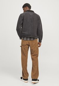Black denim jacket with a corduroy collar, paired with brown corduroy pants featuring pockets. Model stands with back facing the camera.
