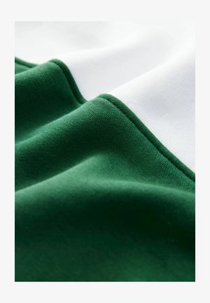 Bomuldsblandet stof med mørkegrønne og hvide sektioner, der har en glat tekstur og rene syninger langs kanterne.