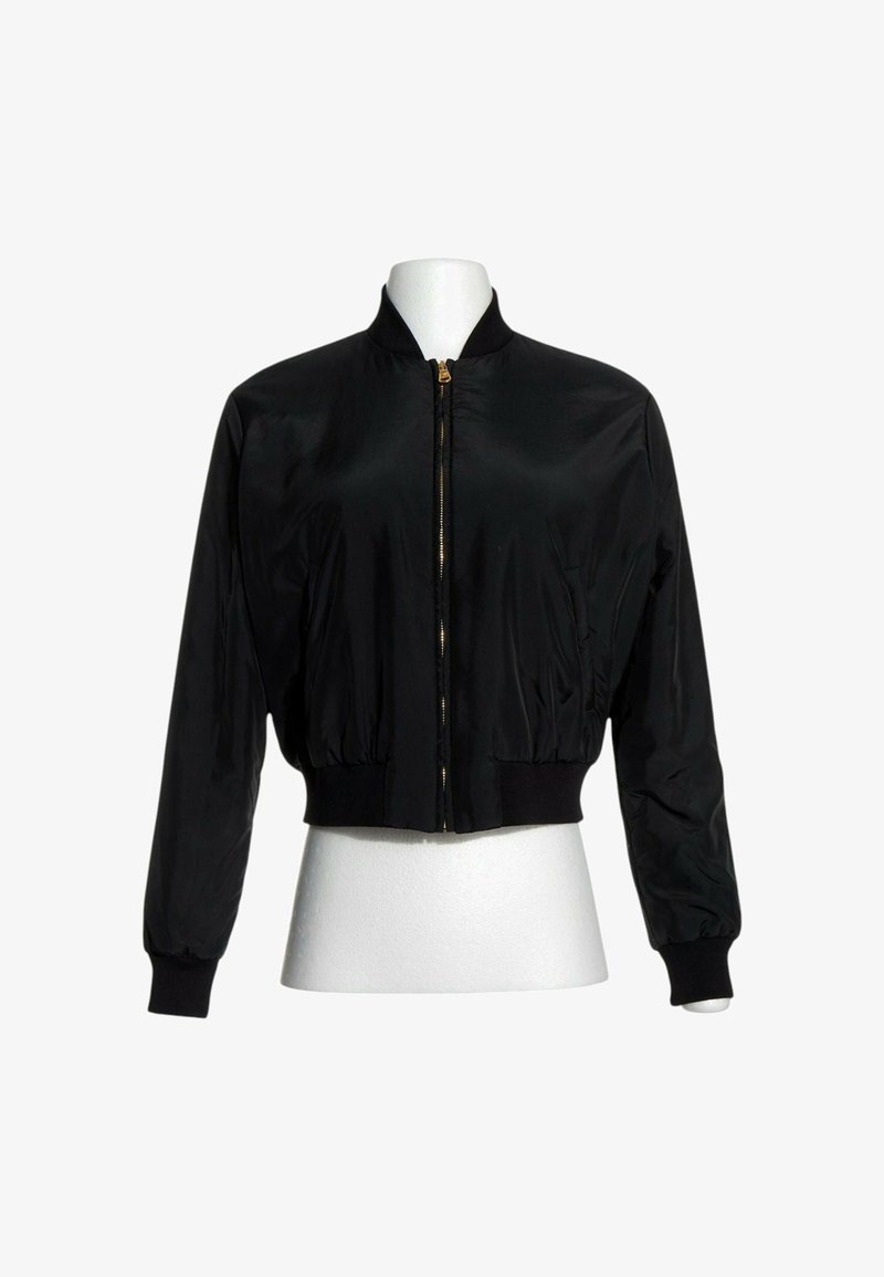 Veste bomber noire avec fermeture éclair sur le devant, col, poignets et taille côtelés, présentée sur un mannequin buste blanc.