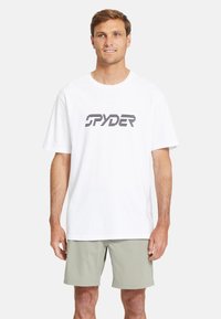 T-shirt bianca in cotone con logo "SPYDER" nero testurizzato, vestibilità comoda, maniche corte e scollatura a girocollo, abbinata a pantaloni corti grigi chiari.