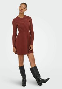 Ribbed dress w kolorze terakoty z długimi rękawami i dopasowanym tułowiem, przechodzącym w rozkloszowaną spódnicę. W połączeniu z czarnymi skórzanymi kozakami do kolan.