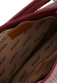 Intérieur d'un sac à main en cuir rouge à pois avec une doublure beige. Comprend une fermeture éclair dorée et le logo "VENEZIA" imprimé plusieurs fois sur la doublure.