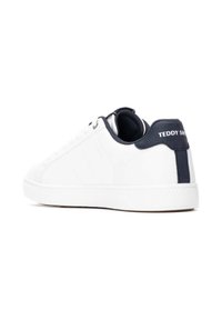 Zapatilla blanca con material de cuero liso, punta redondeada y acentos azul marino en el talón y el cuello. Presenta un sutil detalle texturizado y una marca.