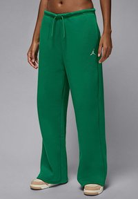 Zielone spodnie dresowe z miękkiego materiału, z regulowanym sznurkiem w pasie, szerokimi nogawkami i małym białym logo Jordan na lewym biodrze.