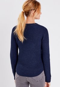 Marineblauer Strickpullover mit langen Ärmeln, gerippter Textur und schmal zulaufendem Saum. Verfügt über einen runden Ausschnitt und dezente Glitzerelemente.