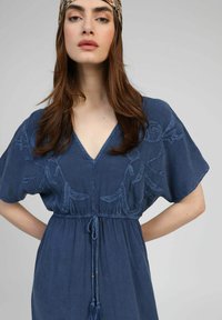 Robe bleue à manches courtes ornée de motifs floraux brodés, d'un décolleté en V, d'une taille ajustable avec cordon et de pompons décoratifs.