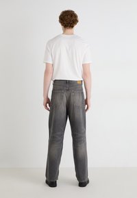 Jean en denim gris avec une jambe droite, doté d'une taille mi-haute, de poches arrière et d'une finition texturée. Associé à un t-shirt blanc uni.