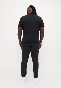Schwarzes kurzärmliges T-Shirt und dunkle Sweatpants, von hinten betrachtet. Glattes Material mit einer taillierten Passform, kombiniert mit weißen Sneakers.