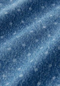 Denim tkanina u različitim nijansama plave s laganim točkastim uzorcima. Tekstura je glatka s mekanim padajem, prikazujući klasičan tkanirani dizajn.
