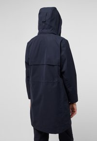 Marine regenjack met capuchon, met een langere achterkant, platte naaddetails en een eenvoudig, functioneel ontwerp dat geschikt is voor nat weer.