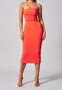 Robe tube moulante de couleur orange vif, texture côtel�ée, silhouette ajustée et longueur mi-mollet. Associée à des sandales à lanières.