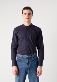 Dark navy long-sleeve shirt with a band collar, button-up front, and smooth texture paired with light blue denim jeans.