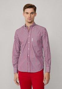 Camisa de botones a rayas rojas y blancas con cuello, mangas largas y un bolsillo en el pecho, hecha de una tela ligera.