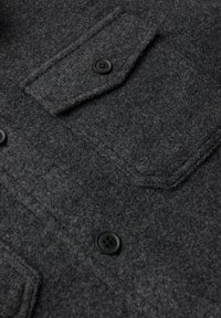 Grå ullskjorta med texturerad finish, med en bröstficka och två svarta knappar för stängning.