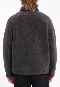 Chaqueta de forro polar topo con una superficie suave y texturizada, presenta un collar con solapa y mangas largas, diseñada para la comodidad y el calor.