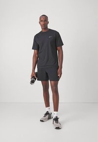 Mustas Nike'i spordiriietuses mees hoiab musta veepudelit, seistes ühtlase helemustal taustal.