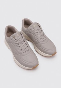 Zapatillas deportivas de color gris claro con parte superior sintética suave, punta redonda, cordones planos y suela de goma con un acento marrón.