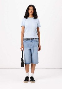 Lyseblå teksturert T-skjorte med kort erme, slitte denimshorts, svarte joggesko med kremfargede såler, og en liten svart veske.