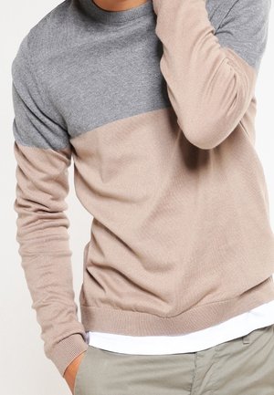 Pull en tricot avec une partie supérieure grise et une partie inférieure beige, doté d'un col rond et de poignets et d'un ourlet côtelés. Texture douce.
