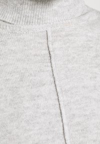 Maglione a collo alto grigio chiaro con una fine trama a coste, dotato di una cucitura centrale che corre lungo la schiena e realizzato in un materiale morbido a maglia.
