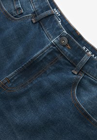 Dunkelblaue Jeans aus Denim mit geradem Schnitt, kupferfarbenen Nähten, Knopfverschluss vorne und fünf Taschen. Lässiger und strapazierfähiger Stoff.